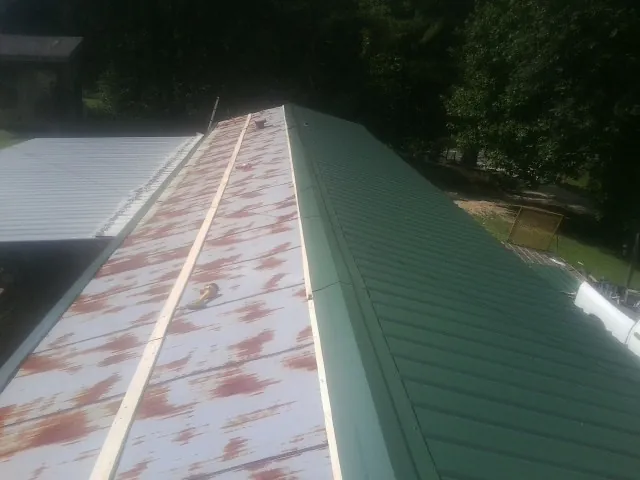 Old rusted panels beside newly installed green metal roofing — Wind Damage Roof Repair by Roofing Brothers in Lamar