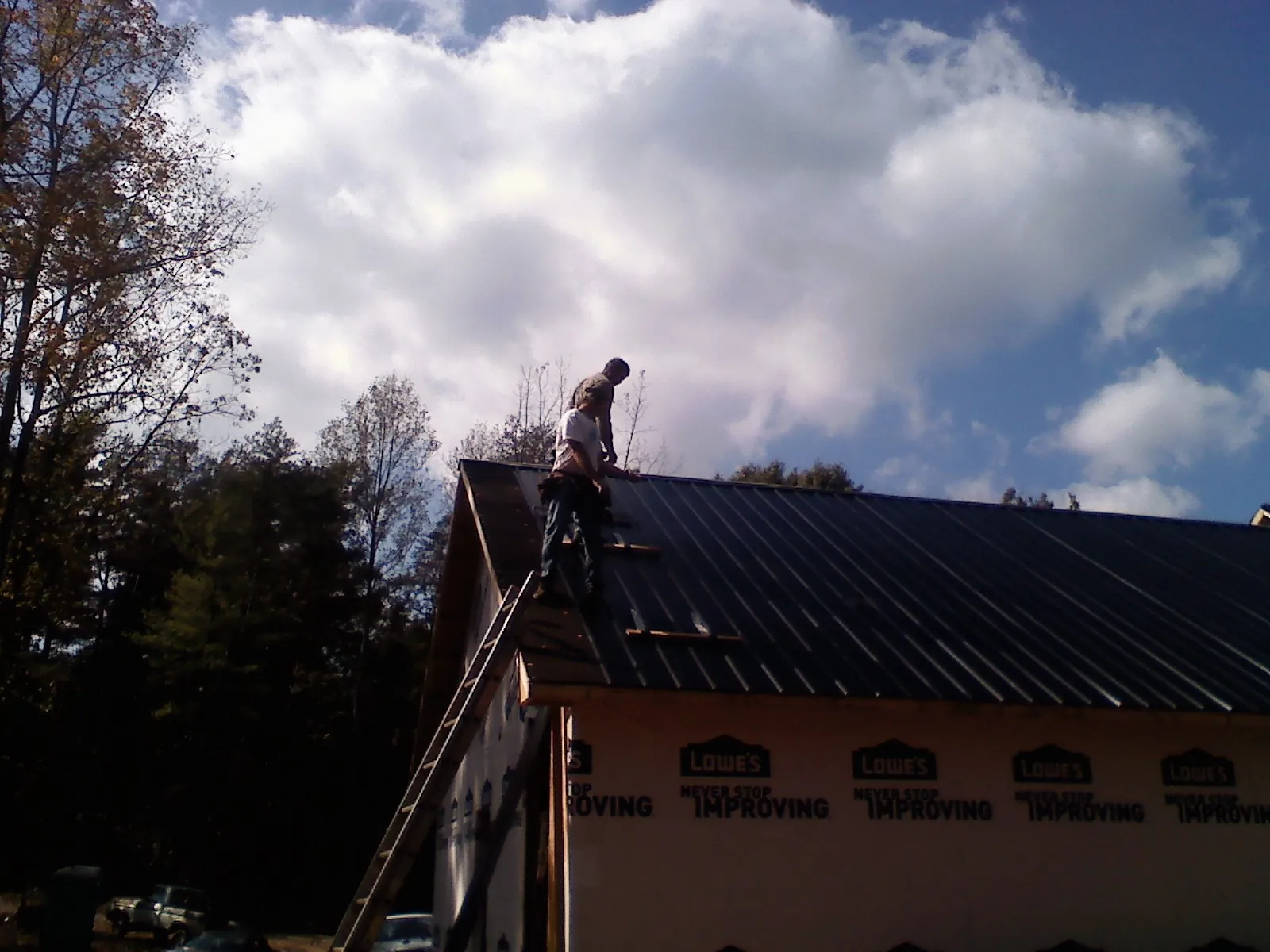 Roofer fastening dark metal panels high against a cloudy sky, from a Roof Inspection job in Lamar